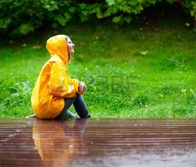 A person wearing a raincoat is sitting in the rain. 