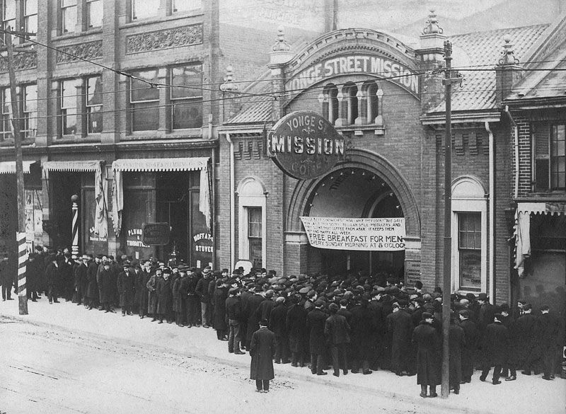 A crowd of men wait outside the doors of a Toronto charity for a meal, 1931.