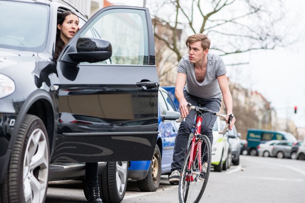 Person opening their car door in front of a bicycle.