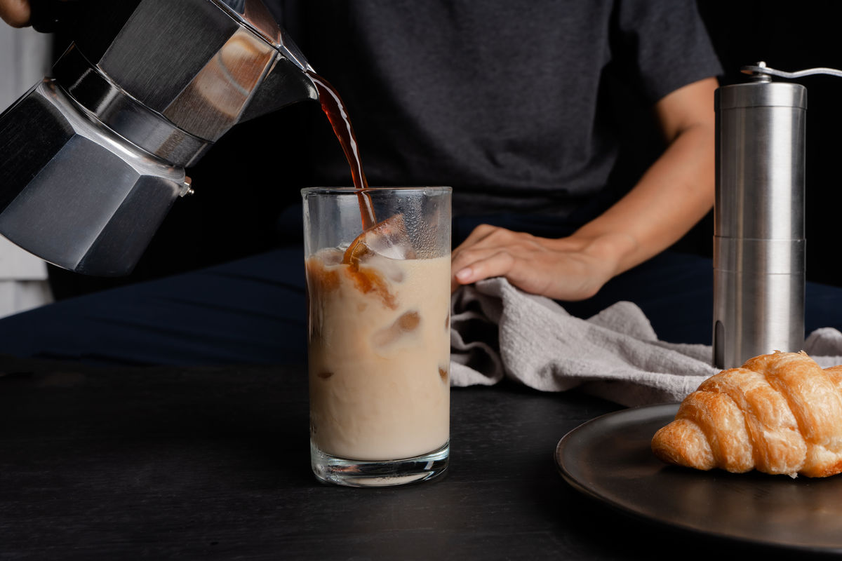 Une personne verse du café chaud dans un verre rempli de glaçons.