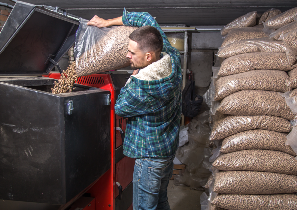 A person emptying a bag of wood pellets into a furnace.