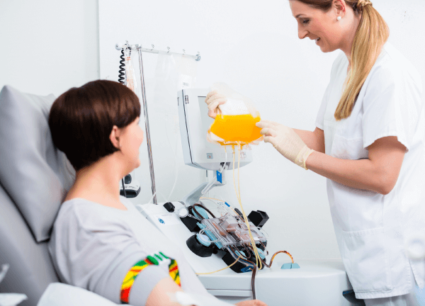 A person accompanied by a health professional makes a plasma donation using an apheresis machine.