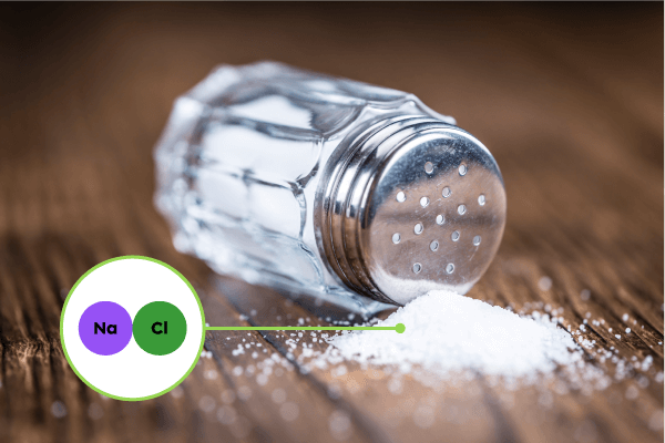 A fallen salt shaker with some salt on a table.