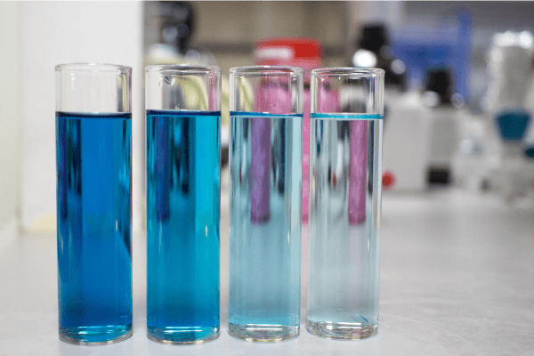 Four test tubes with solutions of different blue shades arranged from darkest (least diluted) to lightest (most diluted).