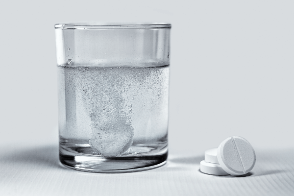 A photograph of a sodium bicarbonate and citric acid tablet that sinks into a glass of water and produces bubbles.