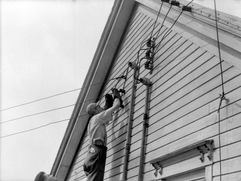 Photographie d’un électricien installant une entrée électrique sur le mur d’une maison de campagne.