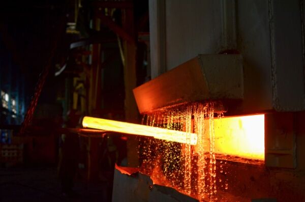 A very hot piece of metal is passed under a stream of cold liquid.