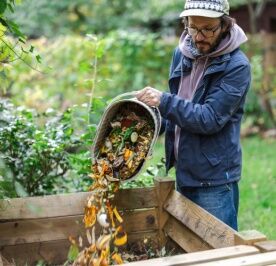 A man throwing vegetable scraps into a compost container.