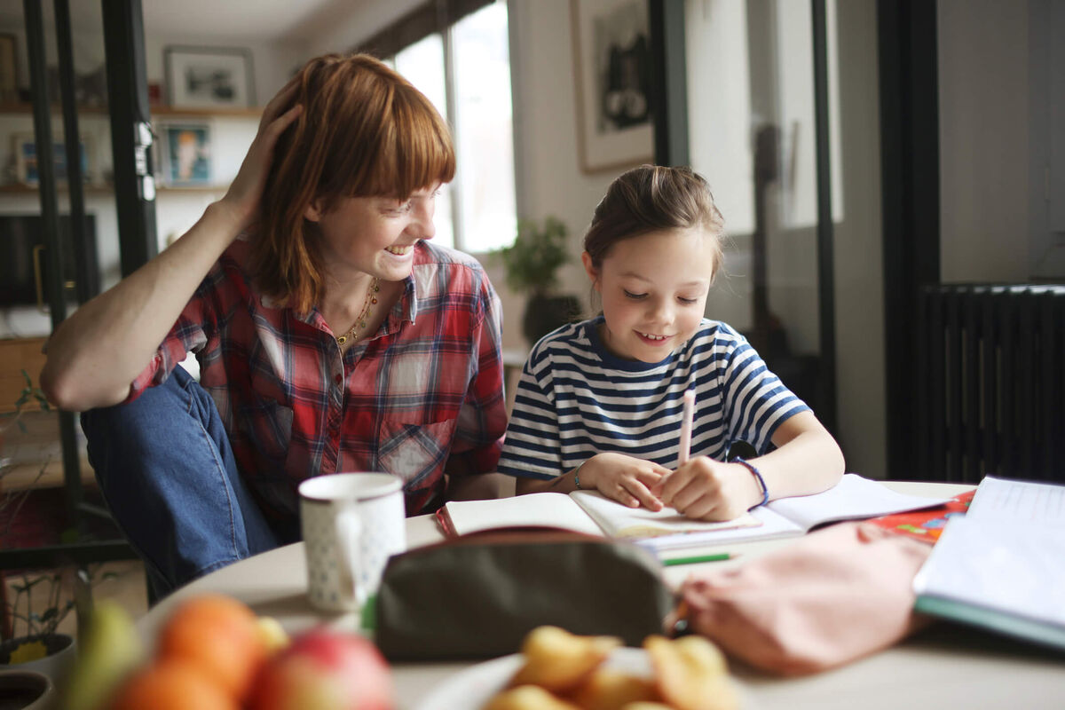 Une mère aidant son enfant à faire ses devoirs.