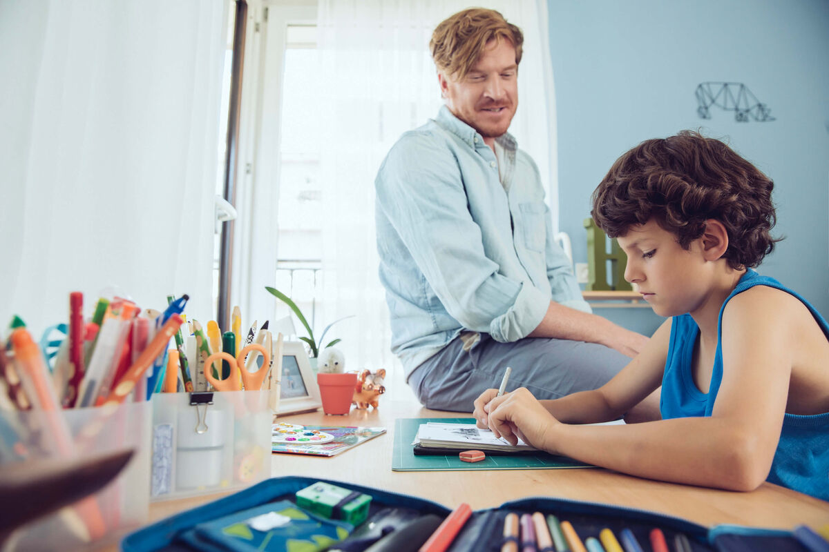 Un père supervisant la séance de devoirs de son fils à la maison.