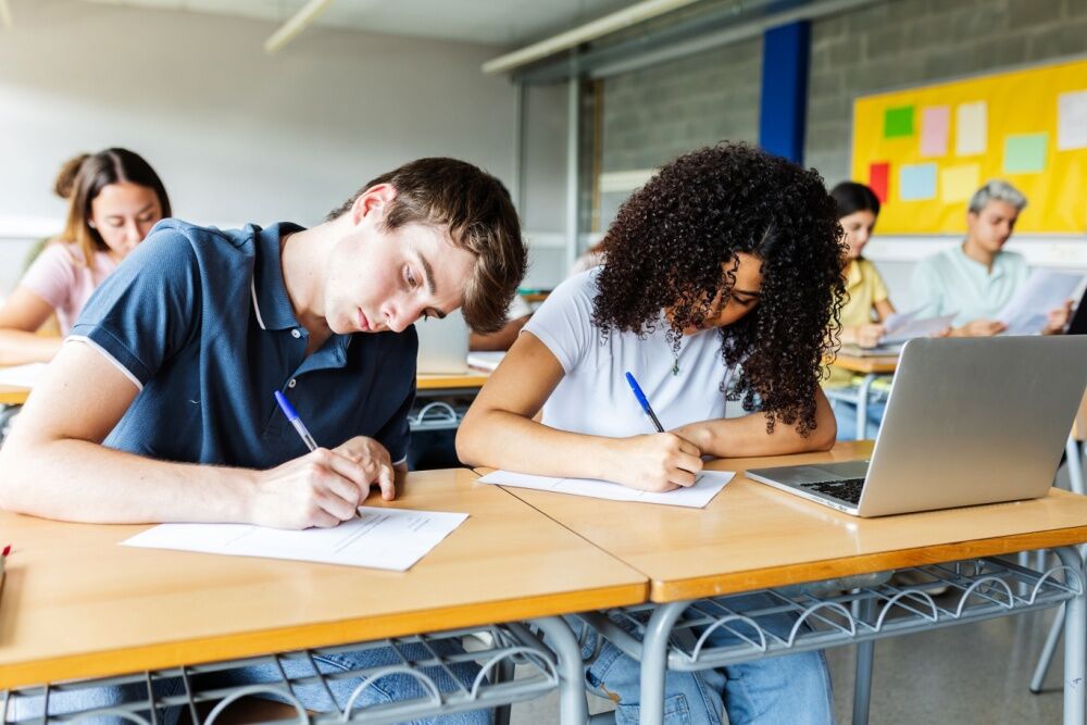High school students in a classroom. One student has a laptop on her desk.