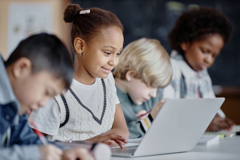 Elementary schoolers in class. One student has a laptop on her desk.